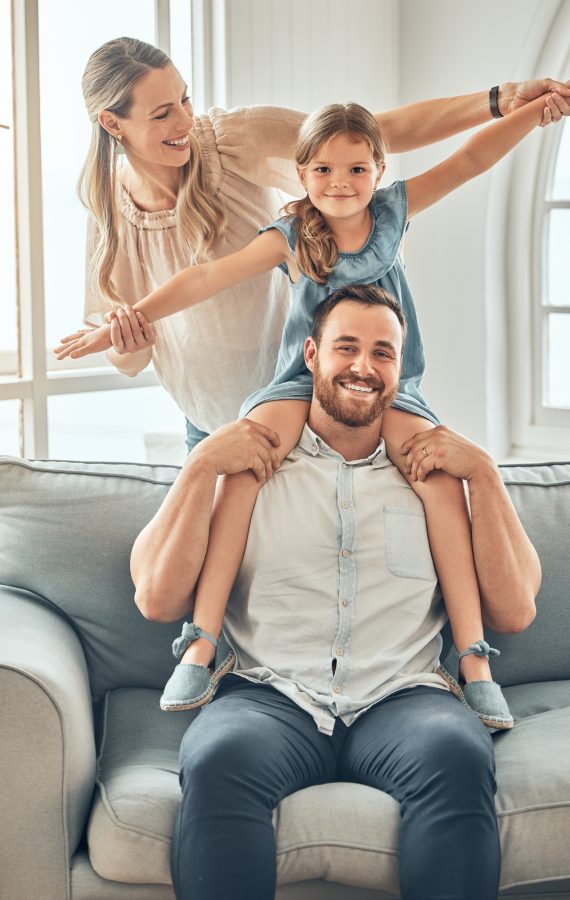Happy young caucasian family bonding with their daughter in the living room at home on the weekend.